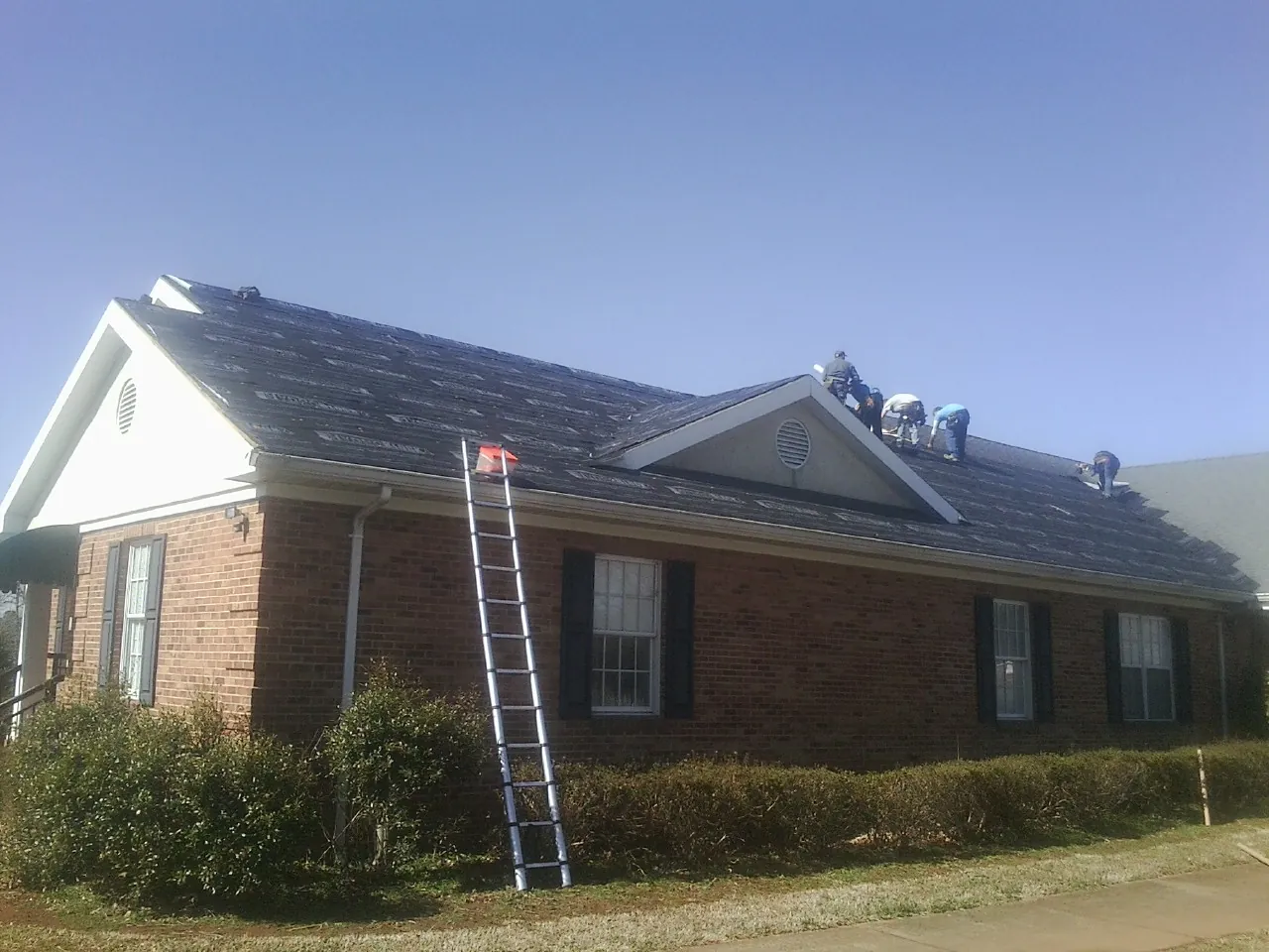Crew tearing shingles off a brick ranch roof with a ladder set — Emergency Roof Repair work by our crew in Chesterton