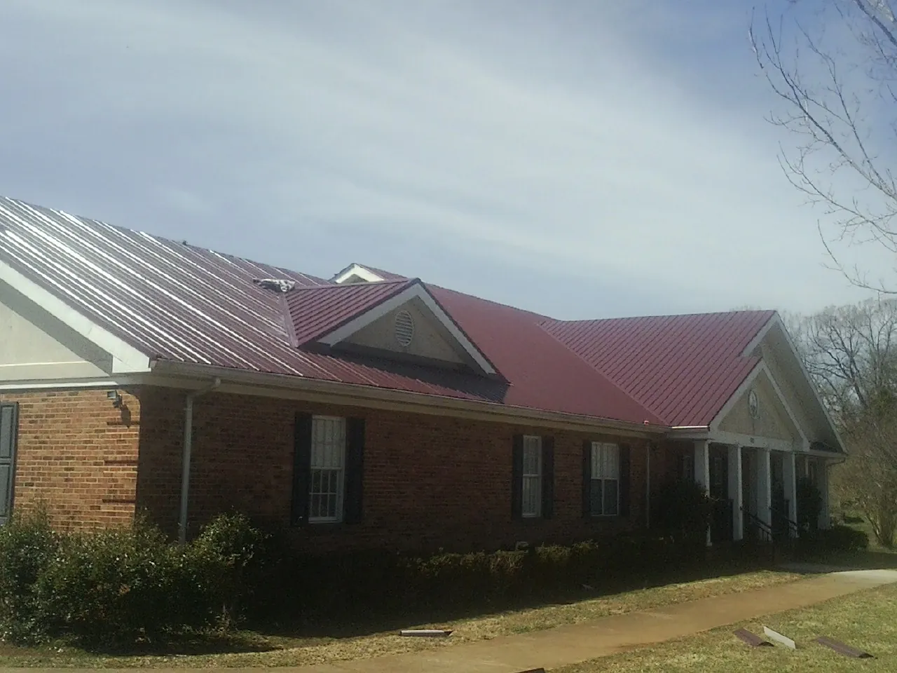Red metal roof with gabled entries on a long brick building, from a Hail Damage Roof Repair job in Chesterton