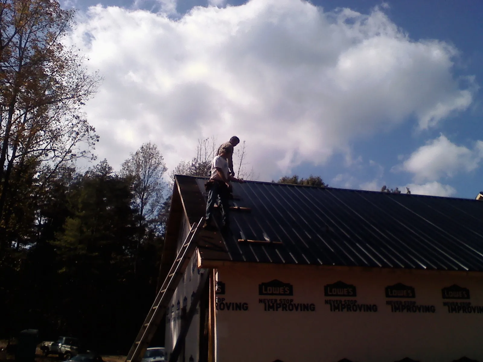 Roofer fastening dark metal panels high against a cloudy sky, from a Roof Inspection job in Chesterton