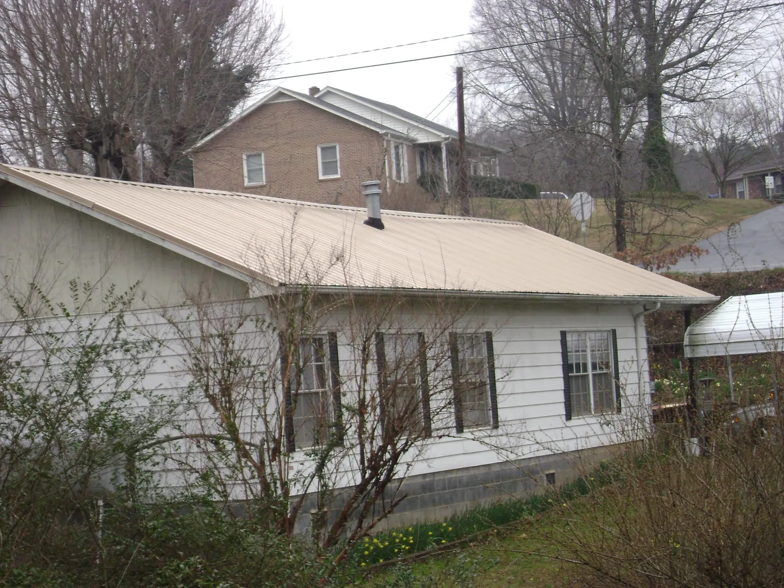 Tan metal roof on a white sided house set into a hillside — Commercial Roofing by Roofing Brothers in Chesterton